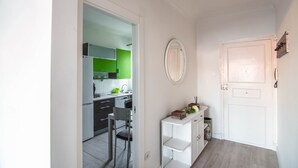 A hallway leading to a kitchen with a green accent wall, a white door, and a small white table with a chair.