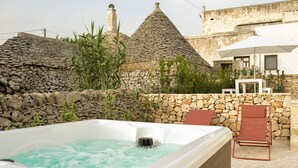 Un jacuzzi en un entorno exterior con paredes de piedra y arquitectura tradicional al fondo.