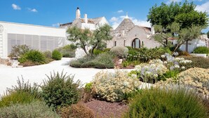 Un edificio de piedra tradicional con tejado de tejas, rodeado por un jardín bien cuidado con diversos arbustos y plantas con flores.