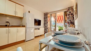 Cocina compacta con armarios blancos, un refrigerador, una mesa de comedor con platos y un televisor.