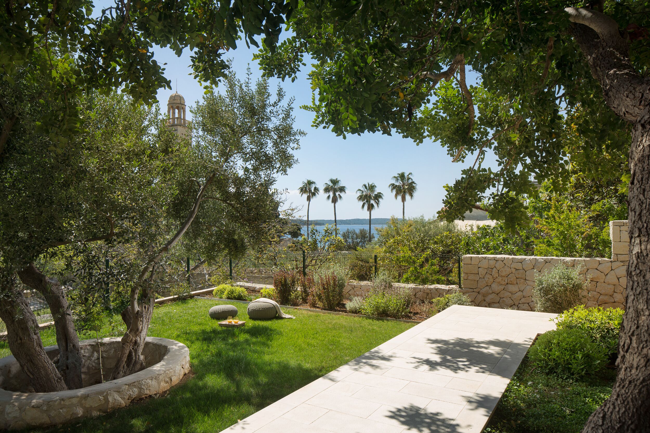 A landscaped garden with a pathway, trees, and a distant view of a body of water.
