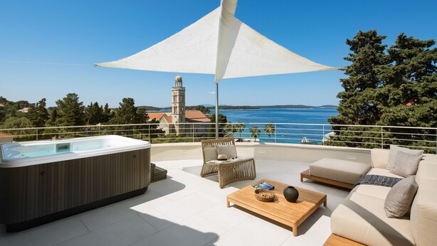 Eine Dachterrasse mit Whirlpool, Sitzgelegenheit und Blick auf das Meer und eine Kirche.