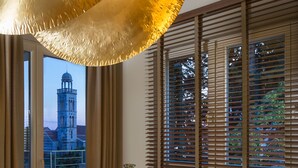 Ein Essbereich mit rundem Tisch, Stühlen, einer Chandelüster und Blick auf einen Turm durch große Fenster.