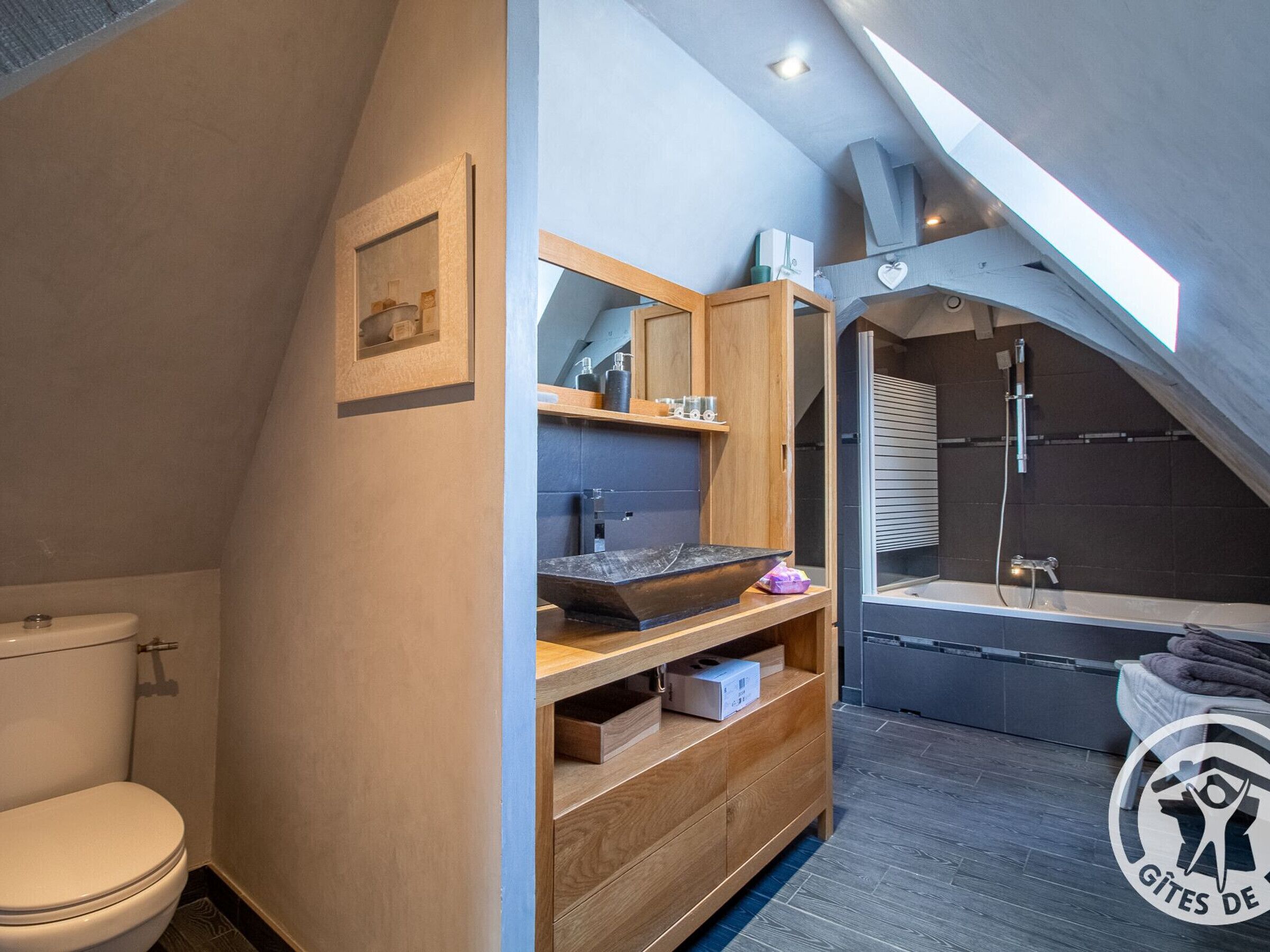 A modern bathroom with a skylight, a wooden vanity, a bathtub, and a shower.