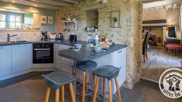 Una cocina con isla central, taburetes de bar y pared de piedra.