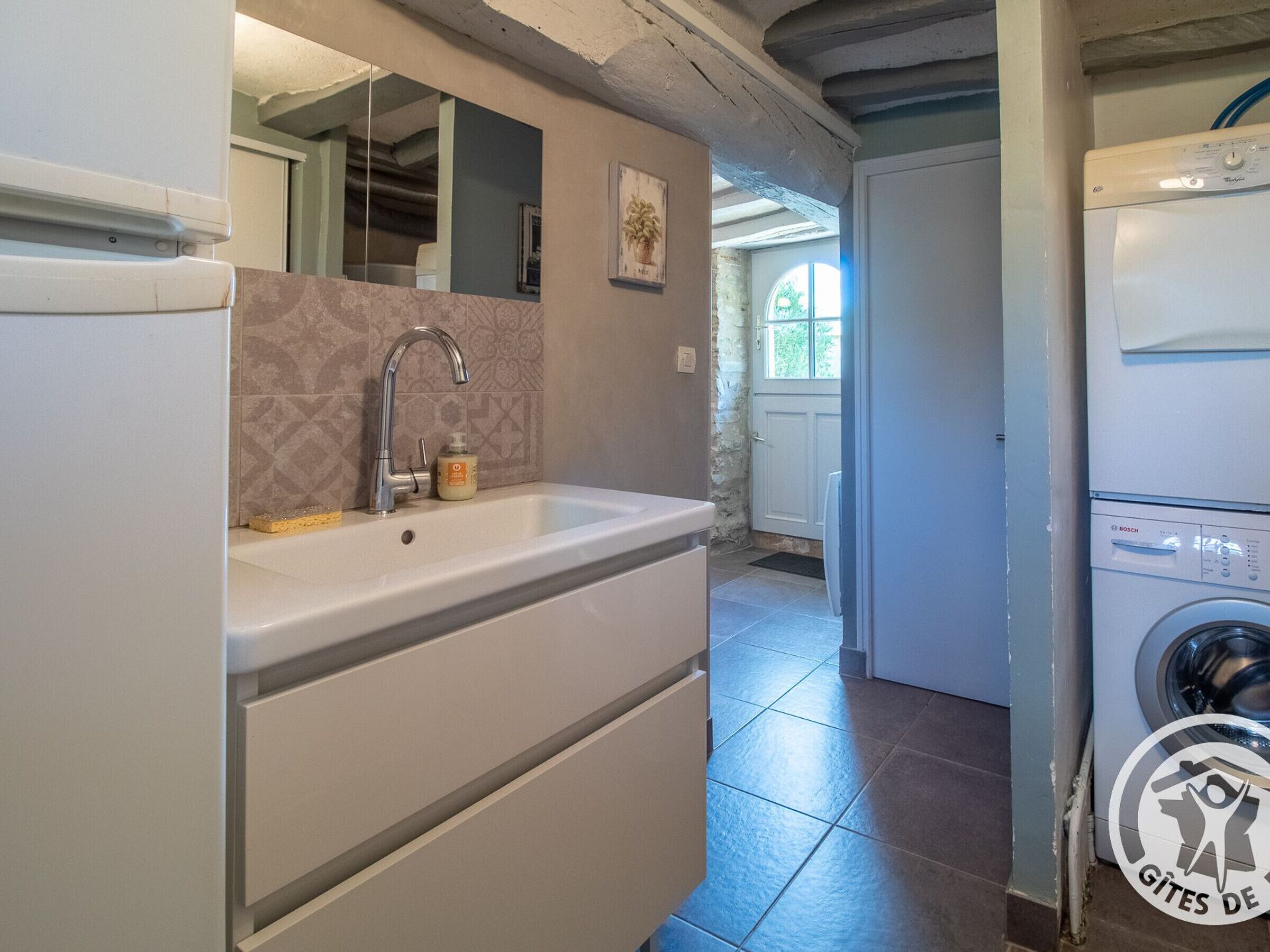 Een badkamer met een wastafel, spiegel en een Bosch wasmachine.