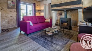Una sala de estar acogedora con pared de piedra, chimenea, sofá y televisor.
