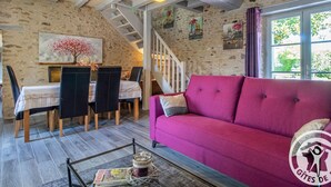 Una sala de estar acogedora con un sofá rojo, una zona de comedor con mesa y sillas, una escalera y una pared de piedra.