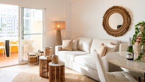 A modern living room with a white sofa, a round mirror, wicker baskets, and a table with a bottle and glasses. - Luxury Beachfront Apartment with Pool in Calpe for 4 Guests (Calpe)