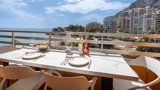 A dining table set for two with a view of the sea and a mountain in the background. - Luxury Beachfront Apartment with Pool in Calpe for 4 Guests (Calpe)