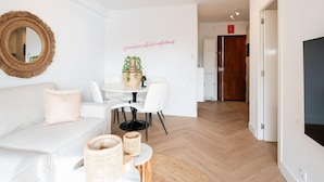 A modern living room with a white sofa, a round mirror, a dining table with chairs, and a potted plant. - Luxury Beachfront Apartment with Pool in Calpe for 4 Guests (Calpe)