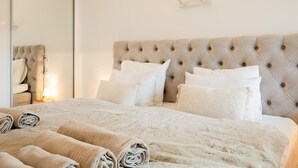 A neatly made bed with a tufted headboard and rolled towels, a bedside table with a lamp, and a mirror on the wall. - Luxury Beachfront Apartment with Pool in Calpe for 4 Guests (Calpe)