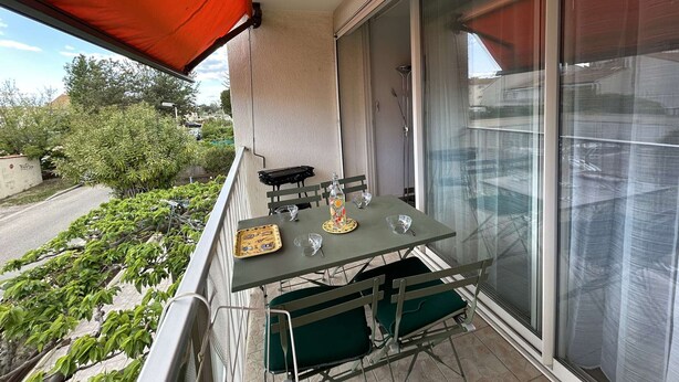 A balcony with a table set for two, a chair, and a small table with a decorative item. - Sunny Duplex with Terrace, A/C, and Garage - Le Grau-du-Roi (Le Grau-du-Roi)