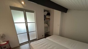 A bedroom with a bed, a sliding glass door, a closet with shelves, and a small table with a fan. - Sunny Duplex with Terrace, A/C, and Garage - Le Grau-du-Roi (Le Grau-du-Roi)