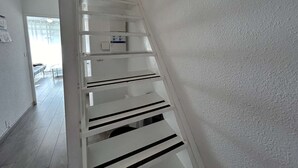 A white staircase with a handrail, leading to a landing with a light switch and a small box. - Sunny Duplex with Terrace, A/C, and Garage - Le Grau-du-Roi (Le Grau-du-Roi)