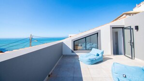 A balcony with a view of the sea, a glass door, and a blue cushion. - Queen of the Bay: Amazing Sea view in the heart of Carvoeiro (Carvoeiro)