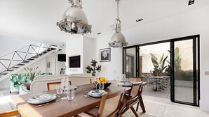 A spacious dining area with a wooden table set for four, surrounded by wicker chairs. A staircase with a geometric design leads to an upper level. - Queen of the Bay: Amazing Sea view in the heart of Carvoeiro (Carvoeiro)