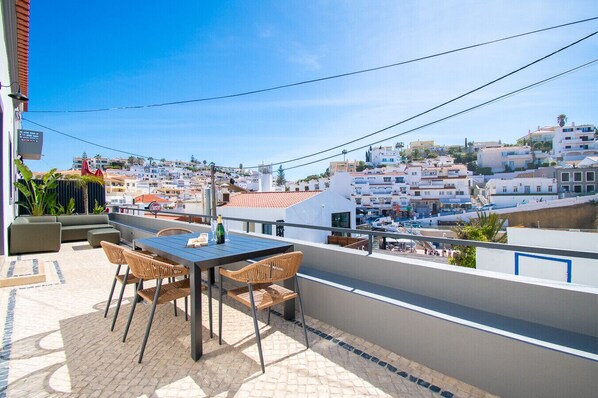 A balcony with a table and chairs, overlooking a coastal town with buildings and a marina.