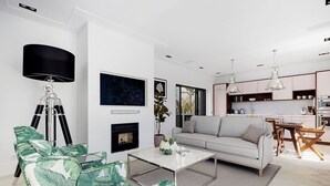 A modern living room with a sofa, coffee table, and a tripod lamp. There is a fireplace, a dining area with a table and chairs, and a kitchen in the background. - Queen of the Bay: Amazing Sea view in the heart of Carvoeiro (Carvoeiro)