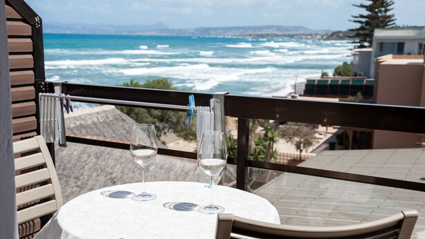 Mesa con dos copas de vino y un mantel, con vistas a una playa y al océano.