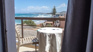 Balcón con mesa y dos copas de vino, con vista al mar y edificios distantes.