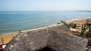 Un resort frente al mar con estructuras de techo de paja, una playa de arena y vista al océano.