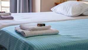 Habitación de hotel con dos camas, cada una con cubrecama azul y almohadas blancas. Hay toallas dobladas en una cama y una botella de loción encima de las toallas.