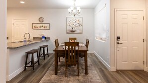 Uma sala de jantar com mesa e cadeiras de madeira, um lustre e um balcão de cozinha com banquetas.