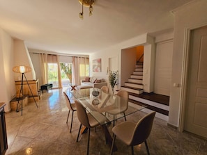Amplia sala de estar con mesa de vidrio para comer, asientos cómodos, una escalera y vistas al exterior.