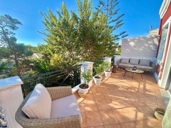 A balcony with wicker furniture, potted plants, and a view of the surrounding area.