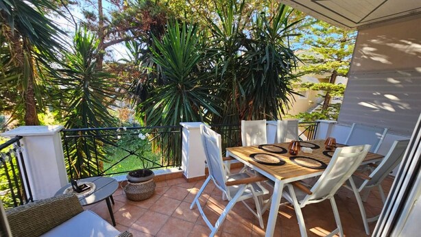 Een balkon met een tafel en stoelen, omringd door planten en een uitzicht op bomen.