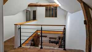 Une pièce de style « loft » avec un plafond en pente, des poutres en bois, une lucarne et un escalier doté d’une rampe en bois.