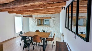 Un coin repas avec une table et des chaises en bois, un mur en pierre et une grande fenêtre.