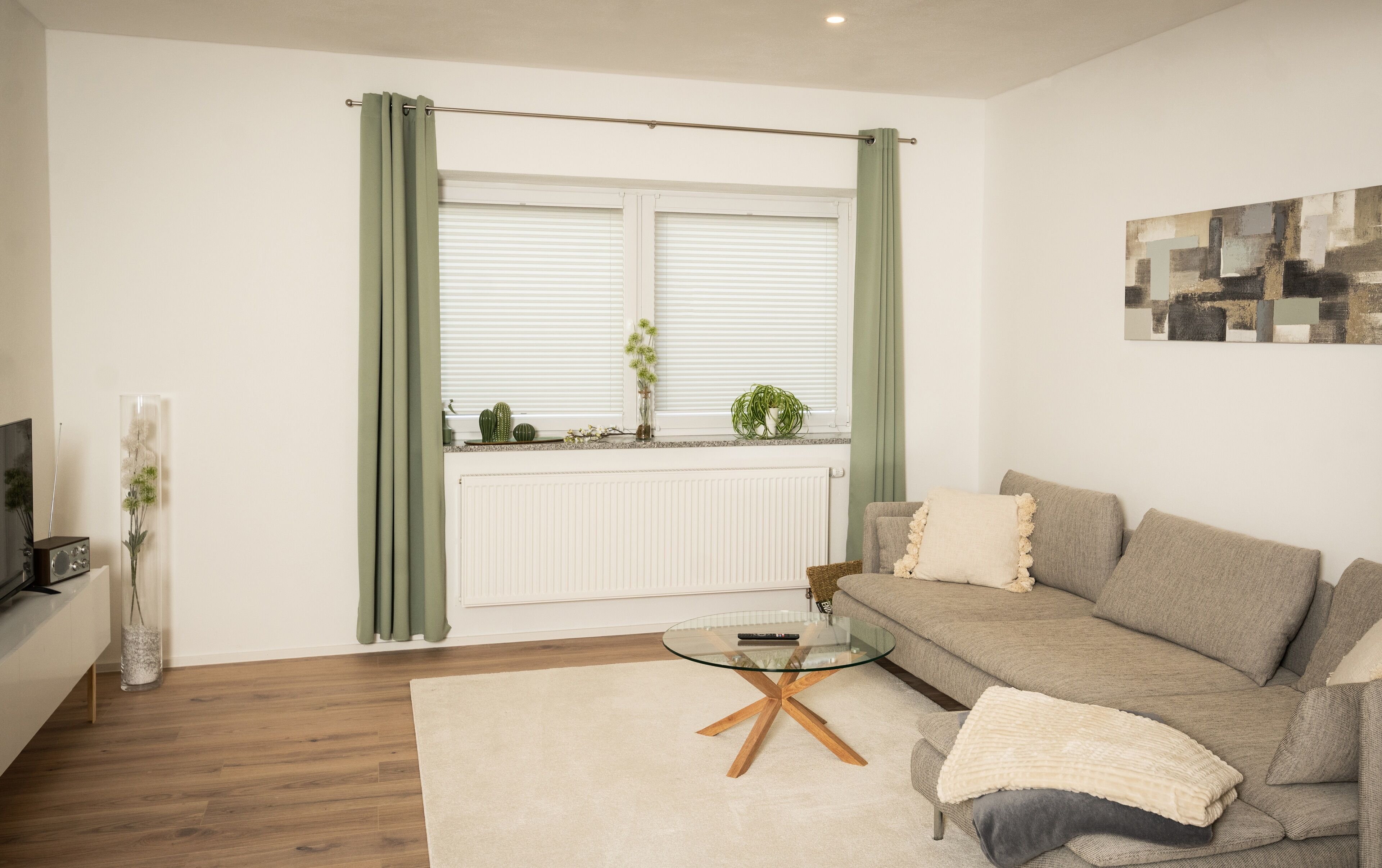 A living room with a sofa, a glass coffee table, a radiator, and a window with curtains.