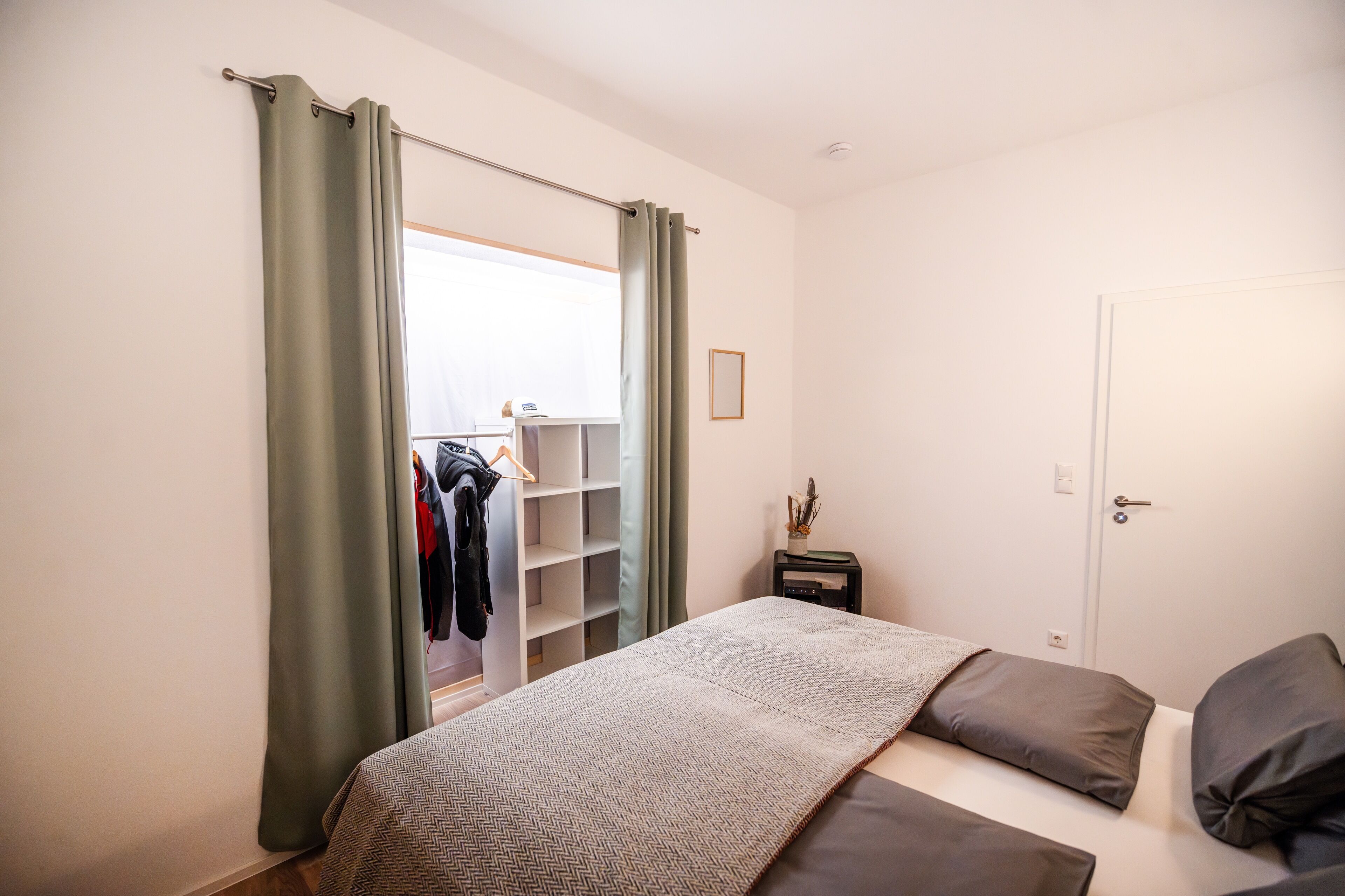 Een slaapkamer met een bed, nachtkastje, kledingkast en een raam met gordijnen.