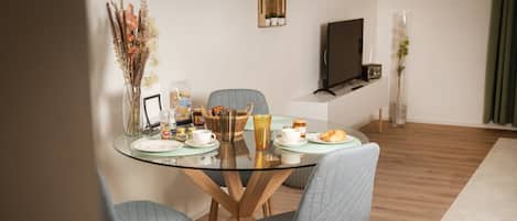 A modern dining area with a glass table, grey upholstered chairs, and a variety of breakfast items.