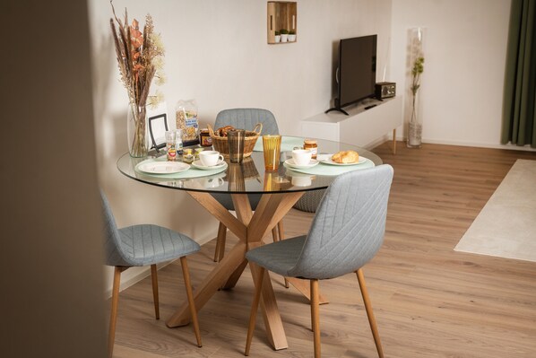 Un comedor moderno con una mesa de vidrio, sillas tapizadas en gris y una variedad de alimentos para el desayuno.