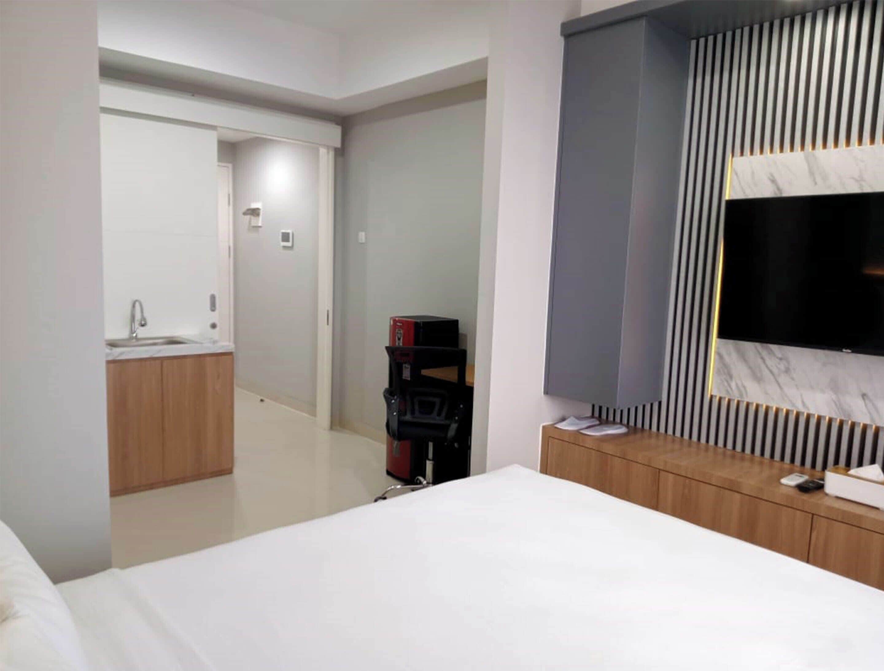 A modern hotel room with a large bed, a TV mounted on the wall, a small desk, and a bathroom visible through an open door.