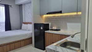 A compact hotel room with a bed, a small kitchenette, and a bathroom. - The Cozy Rooms at The Ayoma Residence (South Tangerang)