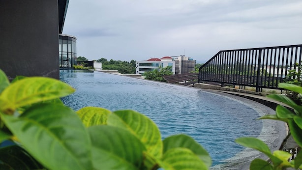 A swimming pool with a curved edge, surrounded by greenery and a black metal fence. - The Cozy Rooms at The Ayoma Residence (South Tangerang)