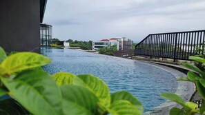 Une piscine à bordures incurvées, entourée de verdure et délimitée par une clôture en métal noir.