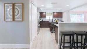 A modern kitchen with dark cabinets, a central island with bar stools, and a view to the outside.
