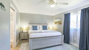 A bedroom with a bed, bedside tables, a ceiling fan, and a view through a window with curtains.