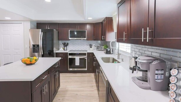 A modern kitchen with dark wood cabinets, a stainless steel refrigerator, a built-in oven, a microwave, and a coffee maker.