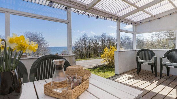 A covered outdoor seating area with a view of the sea, featuring a table with a basket of snacks, a vase of flowers, and two chairs. - 4 bedroom gorgeous home in Allinge (Allinge)