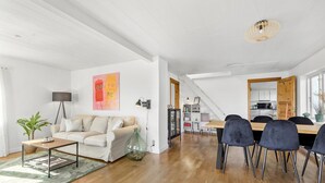 A spacious living area with a sofa, a dining table with chairs, a staircase, and a kitchen in the background. - 4 bedroom gorgeous home in Allinge (Allinge)