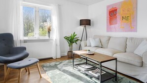 A living room with a grey armchair, a white sofa, a coffee table, a floor lamp, and a large abstract painting on the wall. - 4 bedroom gorgeous home in Allinge (Allinge)