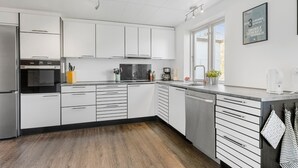 A modern kitchen with white cabinets, a built-in oven, a dishwasher, and a window providing natural light. - 4 bedroom gorgeous home in Allinge (Allinge)