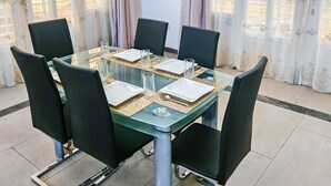 Un comedor con una mesa de vidrio rodeada de sillas negras, dispuesto con platos blancos, vasos y cubiertos.