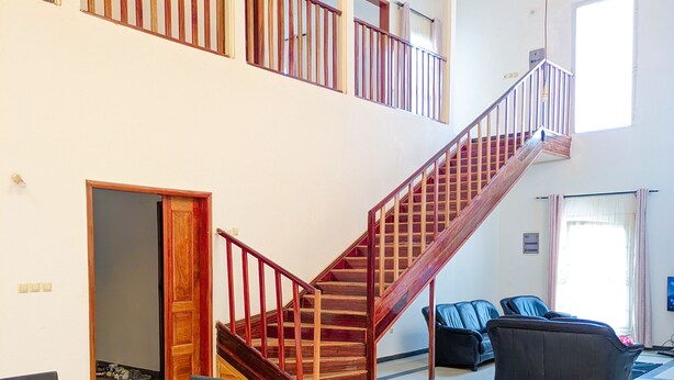 Amplia sala de estar con una mesa de comedor de vidrio, sillas negras, una escalera con barandillas de madera y un sofá de cuero negro.
